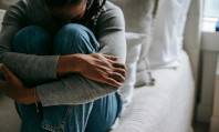Mulher morena de calças de ganga em cima da cama, abraçando as pernas e sentindo ansiedade sexual.